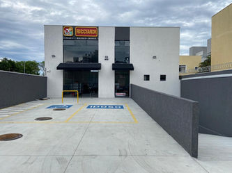 Fachada de obra comercial para loja de venda de massas e alimentos, em cinza com faixas cinza escuro e estacionamento com piso de concreto.
