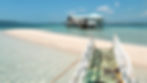 Une Banca accoste sur la bande de sable de Vanishing Island à Davao, avec des eaux turquoise et un ciel clair en toile de fond