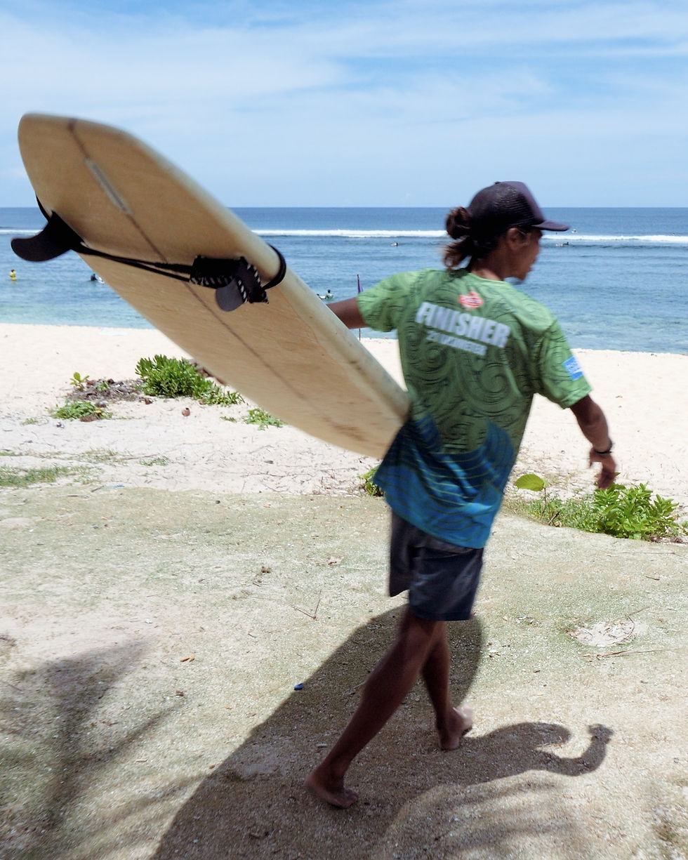 Instructeur de surf marchant sur la plage de Pacifico avec sa planche, Siargao.