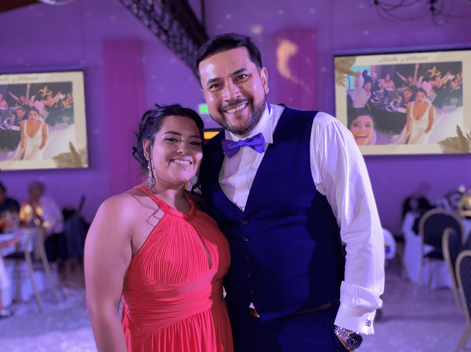 Pareja durante boda elegante celebrando un momento especial mientras invitados comparten recuerdos en tiempo real. Imagen de novios disfrutando su boda con pantalla LED mostrando fotos del evento, ambiente romántico, decoración premium y experiencia interactiva mediante código QR. Ideal para bodas modernas con álbum digital en vivo, RSVP y recuerdos inolvidables compartidos por familiares y amigos.