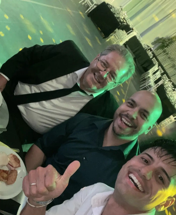 Tres amigos alegres disfrutando una boda elegante, celebrando y compartiendo momentos inolvidables durante el evento. Imagen de grupo de hombres posando, conviviendo y disfrutando la fiesta con pantalla LED transmitiendo fotos en tiempo real y experiencia interactiva mediante código QR. Ideal para bodas modernas con álbum digital en vivo, recuerdos compartidos y momentos especiales entre familiares y amigos.