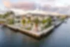 Luxurious waterfront mansion with palm trees, large windows, and patio furniture. Surrounded by calm water under a partly cloudy sky.