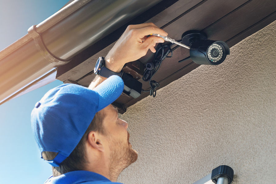 Technician installing an HD surveillance camera under an eave
