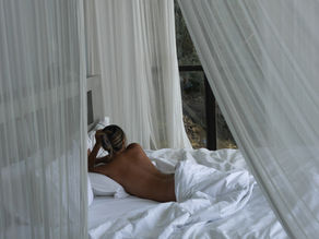 girl laying in bed looking away from the camera. hair is in a clip. it is early morning or evening
