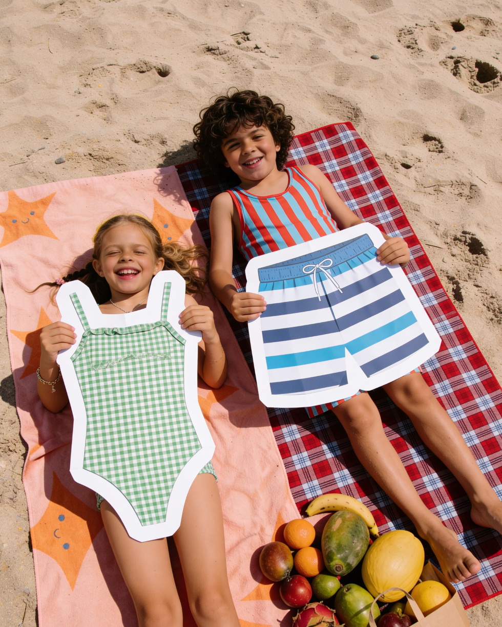 Two children on beach holding swimsuit cutouts.