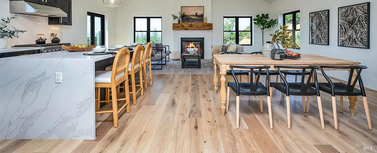 A bright, modern open-concept home featuring premium wide-plank hardwood flooring, a marble waterfall kitchen island, and a cozy fireplace, showcasing the professional installation standards of Harry's Carpets.