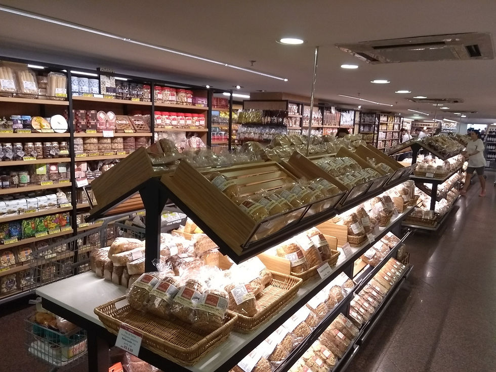 Padaria de supermercado com pães embalados e prateleiras cheias; clientes ao fundo sob luzes quentes.
