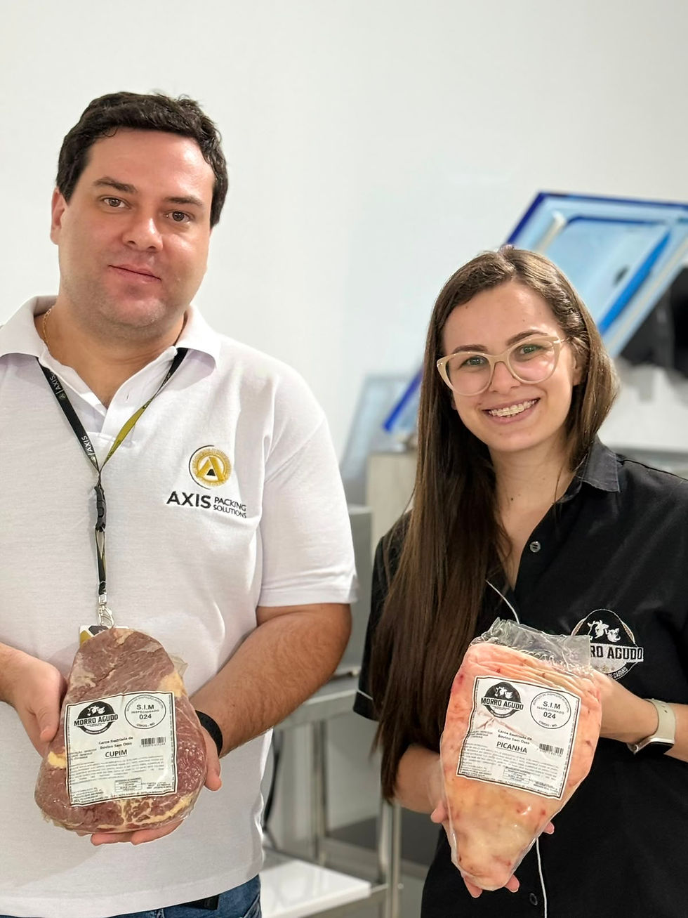 Dois profissionais sorrindo em ambiente interno, segurando embalagens a vacuo de carne Morro Agudo com rótulos Cupim e Picanha.