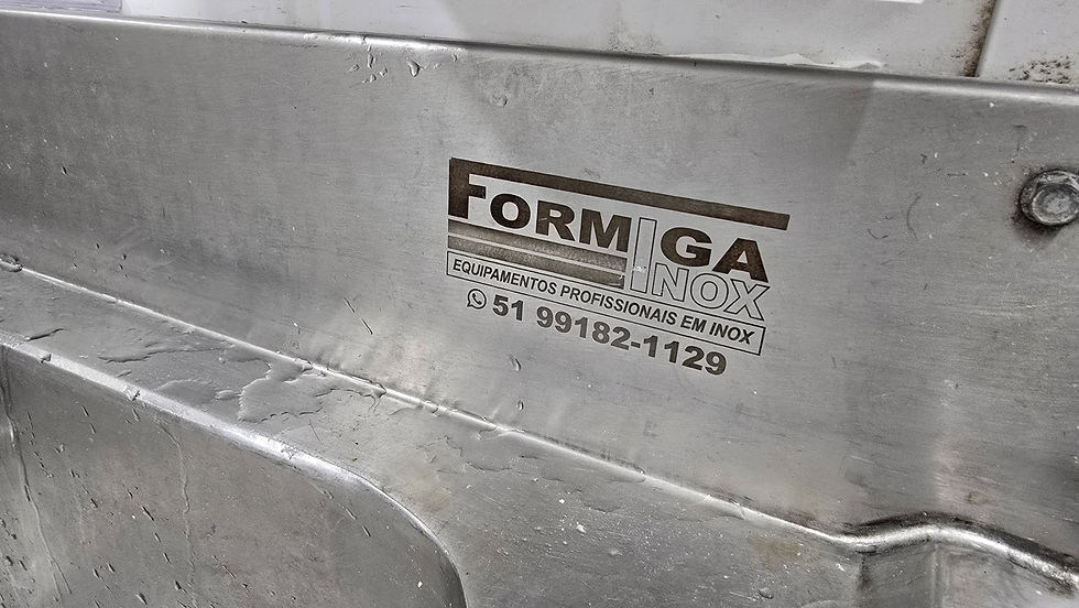 Placa de aço inox com logo da "Formiga Inox", texto "Equipamentos profissionais em inox" e um número de telefone. Fundo cinza.