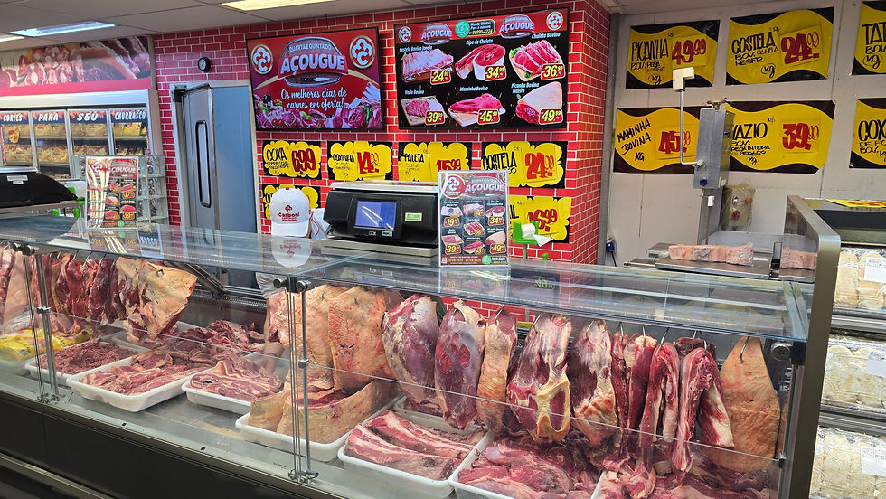 Açougue com carnes expostas em balcão refrigerado, fundo com parede vermelha e placas amarelas com preços promocionais dos cortes.