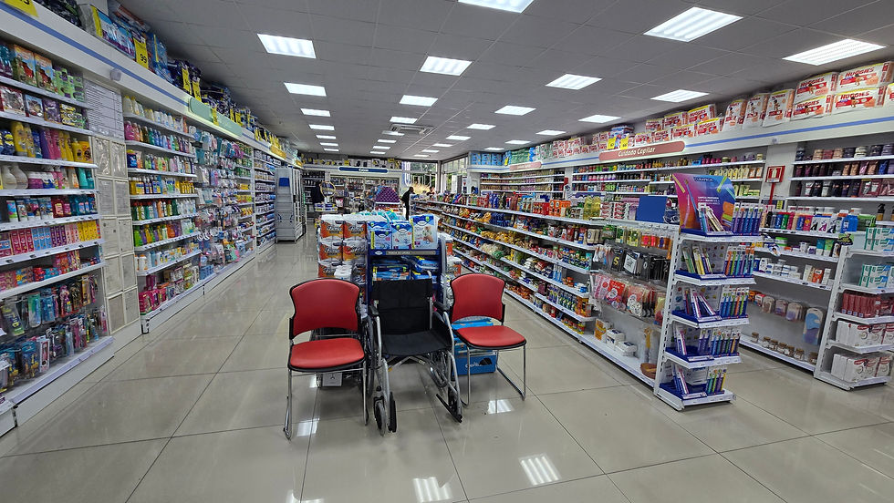Corredor de farmácia bem iluminada, com prateleiras cheias de produtos coloridos. Cadeira de rodas e cadeiras vermelhas no centro.