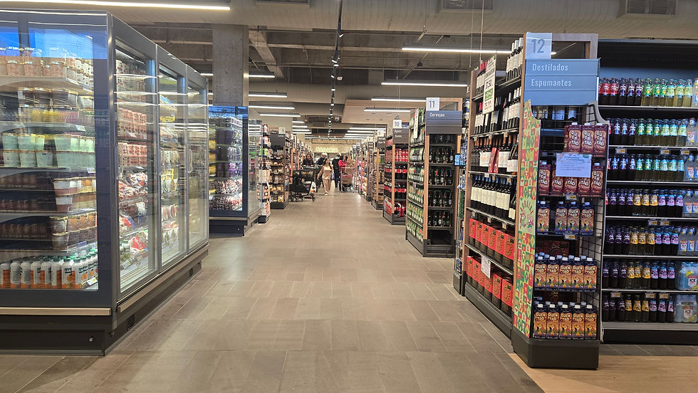 Corredor de supermercado com bebidas e geladeiras; placas 11 e 12, e padaria ao fundo, ambiente iluminado.