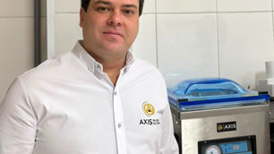 Abílio Corrêa - especialista em embaladoras e embalagens a vácuo, termoencolhimento e atmosfera modificada. É CEO e fundador da AXISVAC e vice-presidente regional da Associação Mineira de Supermercados - AMIS ao lado de uma máquina AXIS inox, em ambiente de azulejos brancos, com expressão calma.