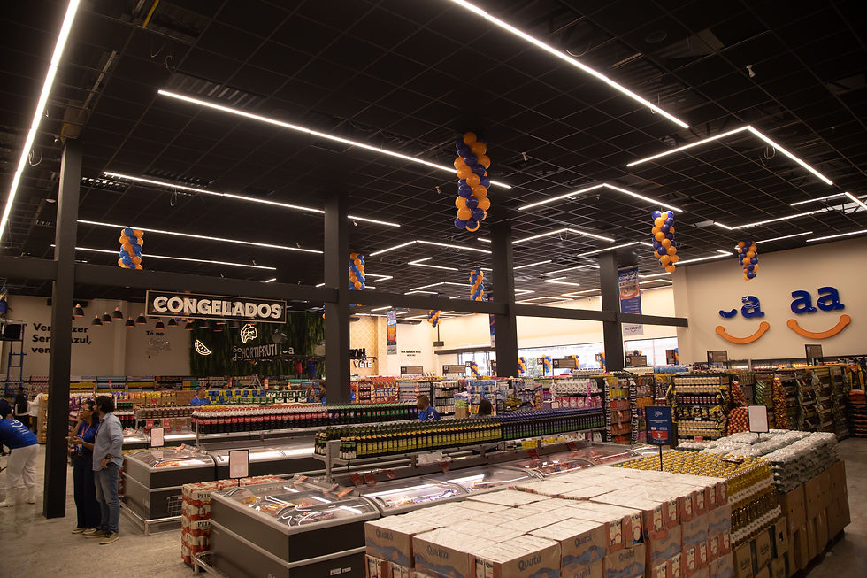 Supermercado iluminado com corredores cheios, funcionários e clientes, balões azul e laranja e placas como CONGELADOS.