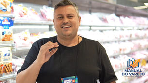 Júnior Silva do Manual do Varejo sorridente em supermercado, gesticulando, com prateleiras ao fundo e logo Manual do Varejo Consultoria & Gestão.