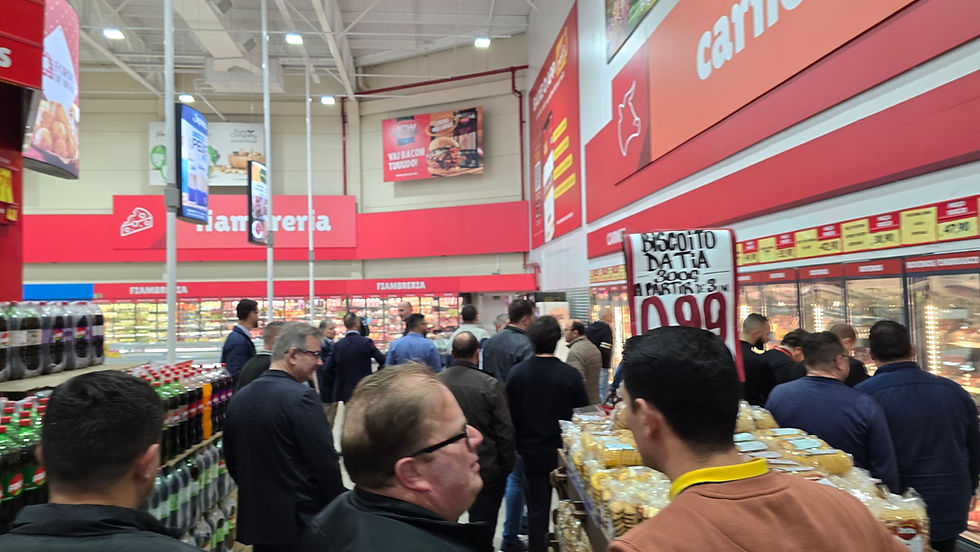 Clientes em fila num supermercado, entre bebidas e frios, com placas de oferta e preço 0,99 em vermelho.