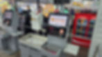 Caixas de autoatendimento em supermercado, self-checkout, com telas Supermercado Madi, sacolas brancas e geladeira Coca-Cola ao fundo.