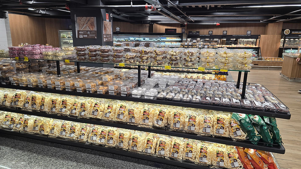 Supermercado com prateleiras cheias de petiscos e biscoitos embalados, em cores variadas, sob luzes, ambiente organizado.