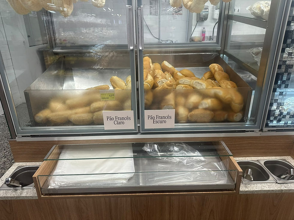Vitrine de padaria com pães franceses claros e escuros, etiquetas visíveis e bandeja vazia ao centro.