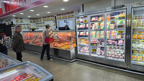 No açougue de supermercado, dois clientes escolhem carnes em vitrines geladas com promoções em placas amarelas.