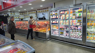 No açougue de supermercado, dois clientes escolhem carnes em vitrines geladas com promoções em placas amarelas.