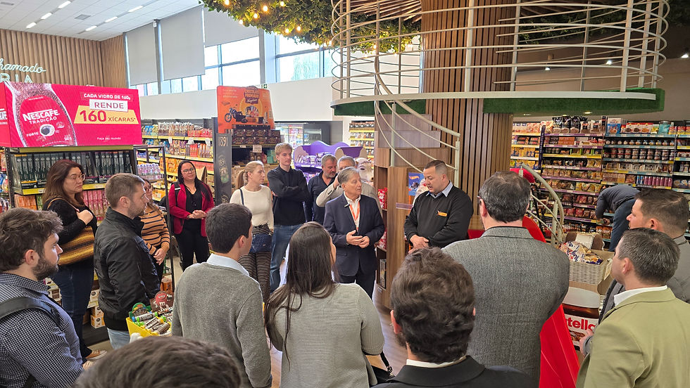 Grupo de pessoas em supermercado, concentradas em uma apresentação. Prateleiras de produtos ao fundo e placa vermelha com texto "NESCAFÉ".