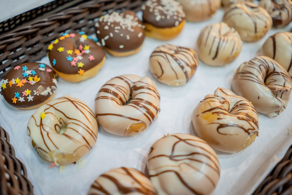 Donuts decorados com coberturas de chocolate e confeitos coloridos em uma bandeja de papel branco. Atmosfera apetitosa e divertida.