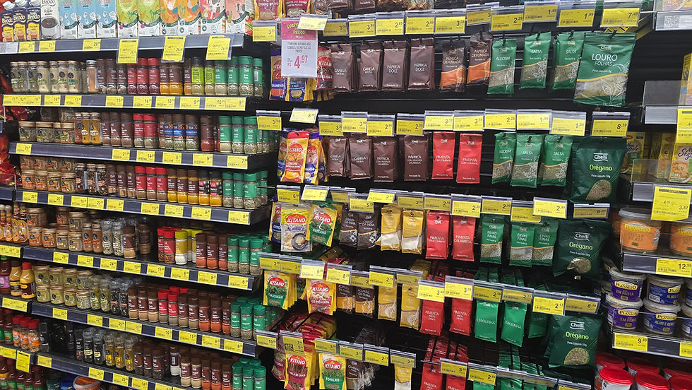 Corredor de supermercado com temperos e especiarias em potes e sachês coloridos, etiquetas de preço amarelas e clima organizado.