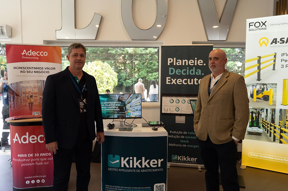 Ricardo Romanetto e Marcelo Vinhas em um stand de evento, cercados por banners da Adecco e Kikker. Tela exibe texto: “Planeie. Decida. Execute.” Ambiente profissional.