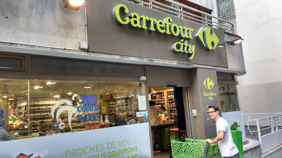 Fachada do Carrefour City com letreiro verde; homem de óculos empurra carrinho verde na entrada, com produtos e luzes ao fundo.