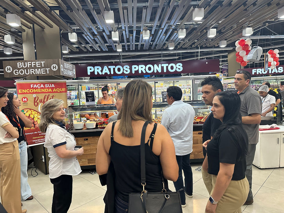 Pessoas em fila diante de buffet gourmet em supermercado, com placas PRATOS PRONTOS e FAÇA SUA ENCOMENDA AQUI.