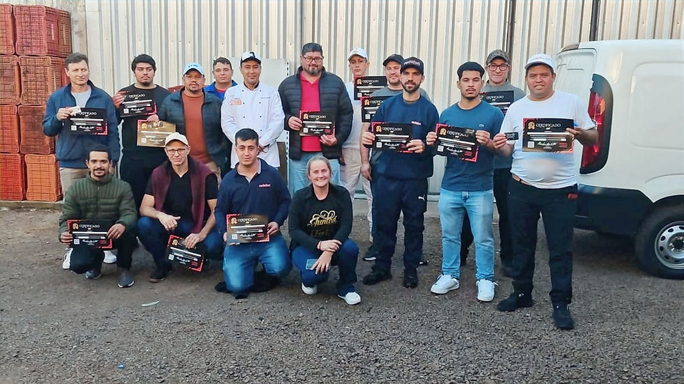 Grupo de 13 pessoas posa com certificados diante de uma van branca e caixas empilhadas, em ambiente industrial.