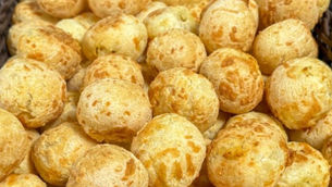 Cesto de pães de queijo dourados com logo Valochi Sousa Pães Congelados sobre cestos de vime.