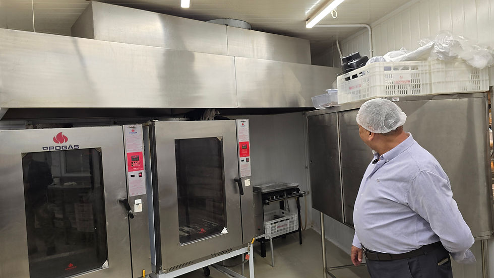 Homem com touca inspeciona cozinha industrial com fornos inox da marca Progás. Ambiente limpo e organizado com cestos no alto.