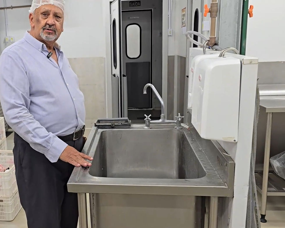 Homem de camisa azul e touca está ao lado de uma pia de inox em uma cozinha industrial. Porta com escrita "SAÍDA" ao fundo.