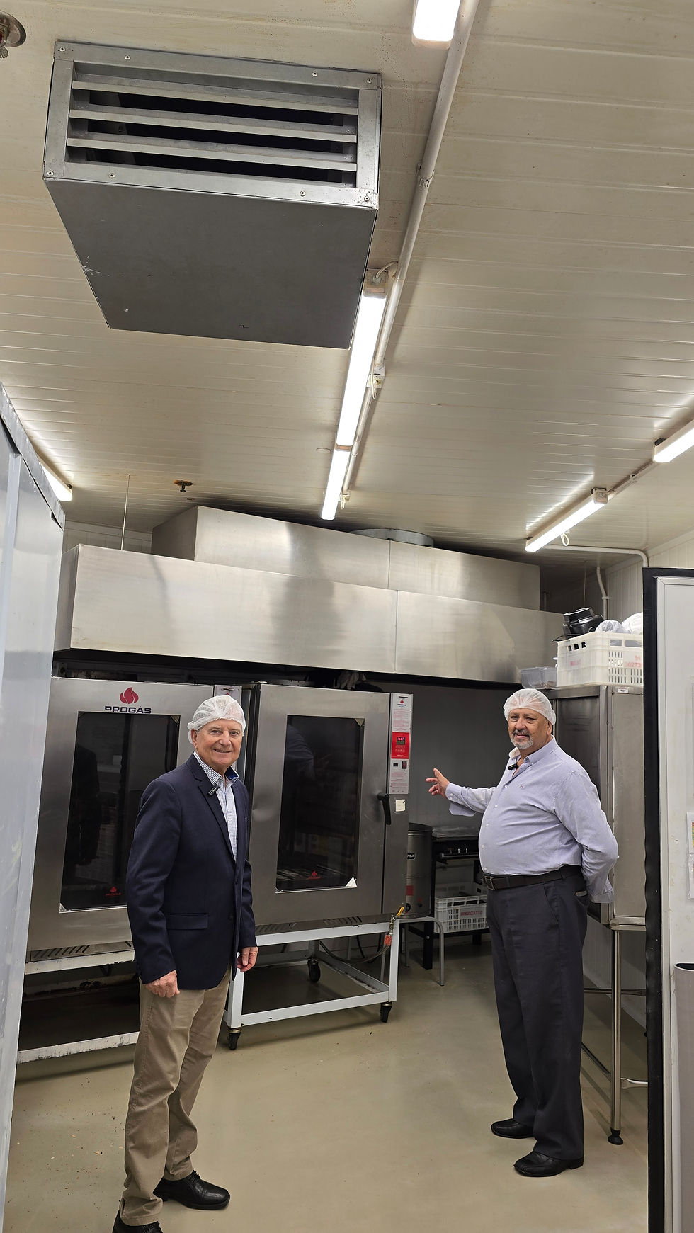 Dois homens em uma cozinha industrial, usando tocas, posam sorrindo. Ao fundo, forno de aço inoxidável com logotipo "Opogás".