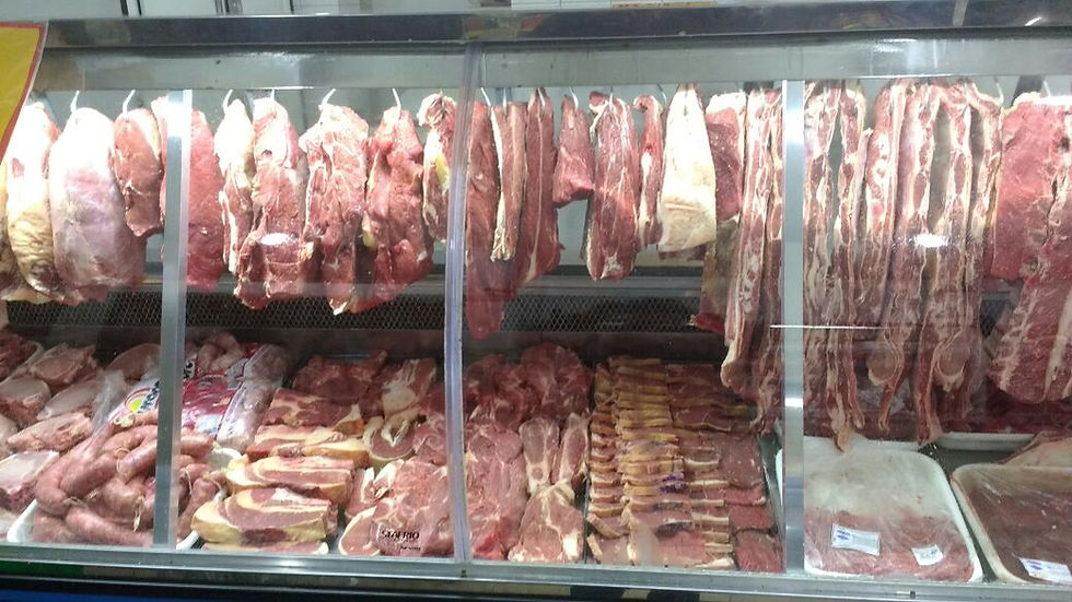 Vitrine de açougue cheia de carnes cruas penduradas e em bandejas, com tons de vermelho e branco, ambiente de mercado.