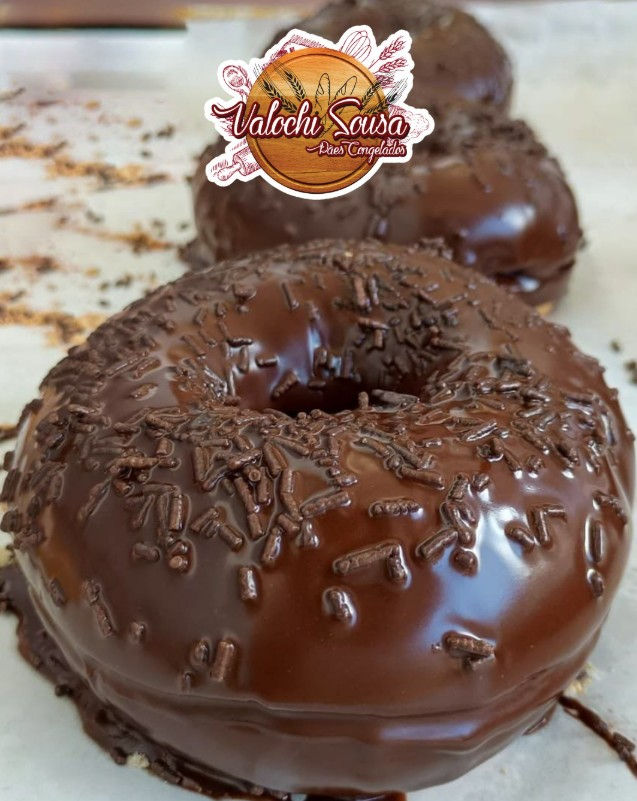 Donuts cobertos com granulado de chocolate em fundo desfocado. Logo "Valochi Sousa Pães Congelados" no topo. Atmosfera apetitosa.