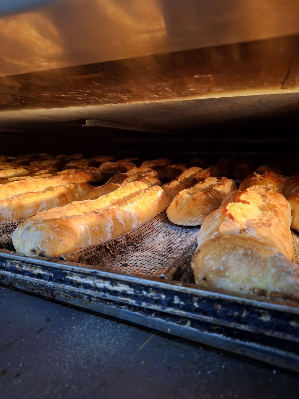 Baguetes douradas assando em forno quente, destacando-se sobre uma grade metálica. Ambiente acolhedor e aroma tentador de pão fresco.