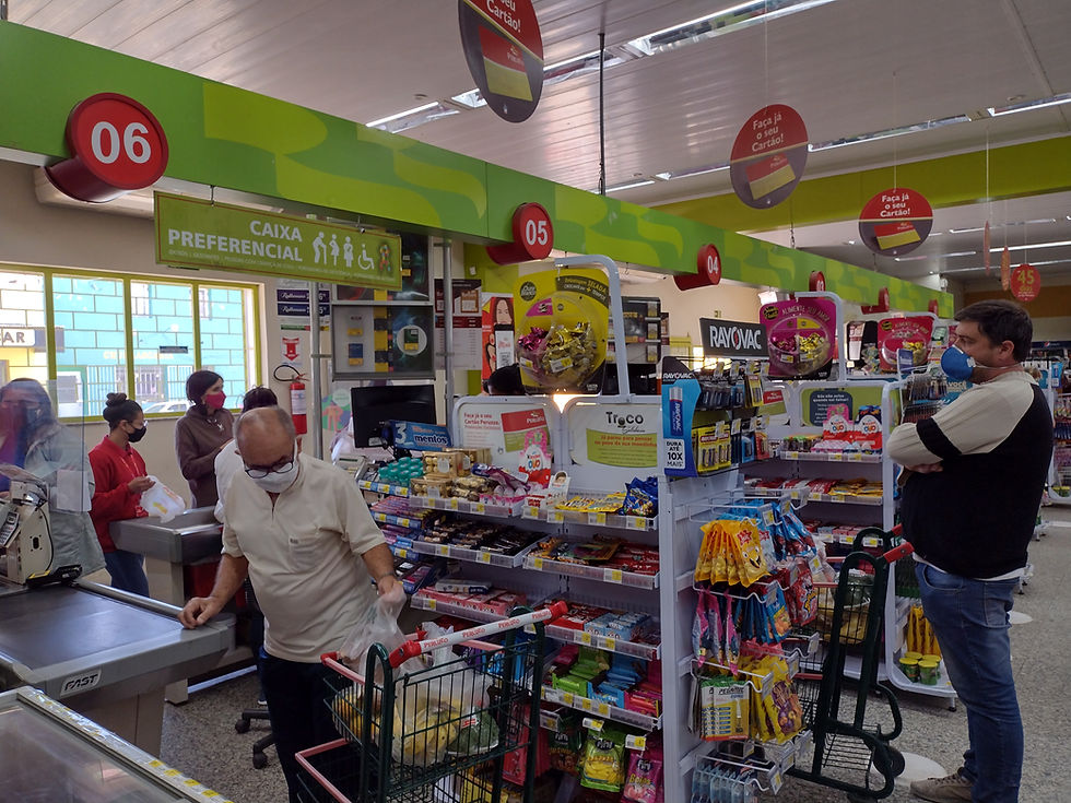 Corredor de loja com chinelos e pantufas coloridos em exposição, placas de promoção amarelas e carrinho, clima de varejo movimentado.