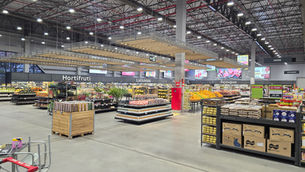 Interior de supermercado amplo e moderno, com hortifruti, laticínios, açougue e ovos expostos sob teto alto e luminoso.