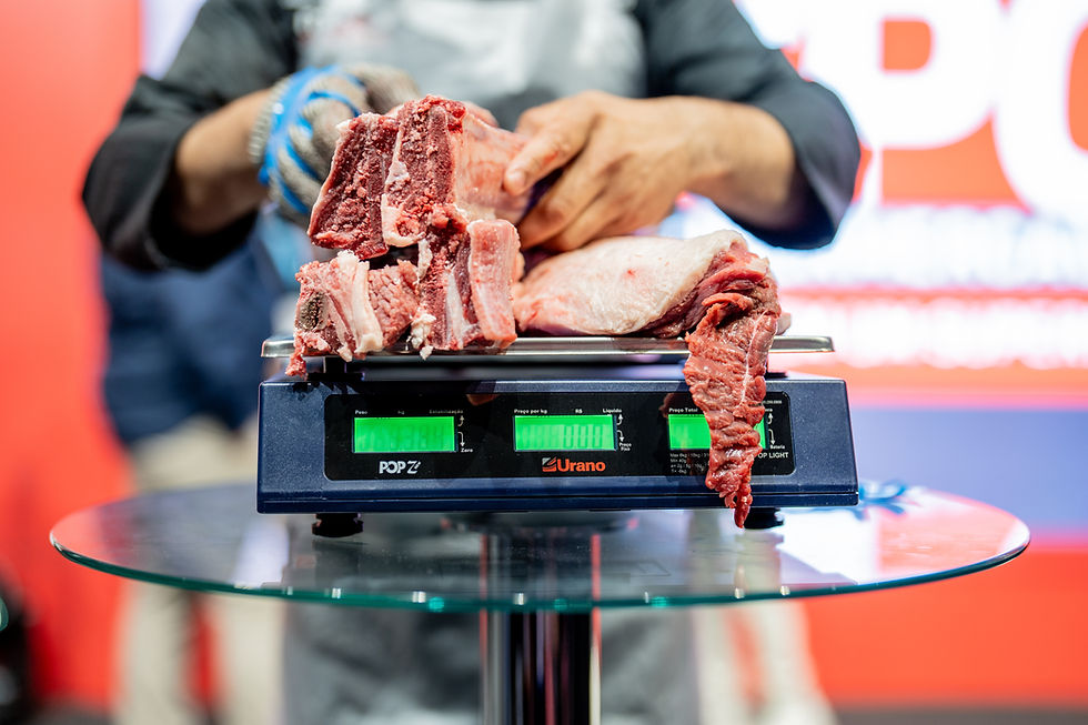 Carne crua sendo pesada em balança digital Urano. Mãos ajustam os pedaços. Fundo desfocado vermelho e branco, atmosfera profissional.