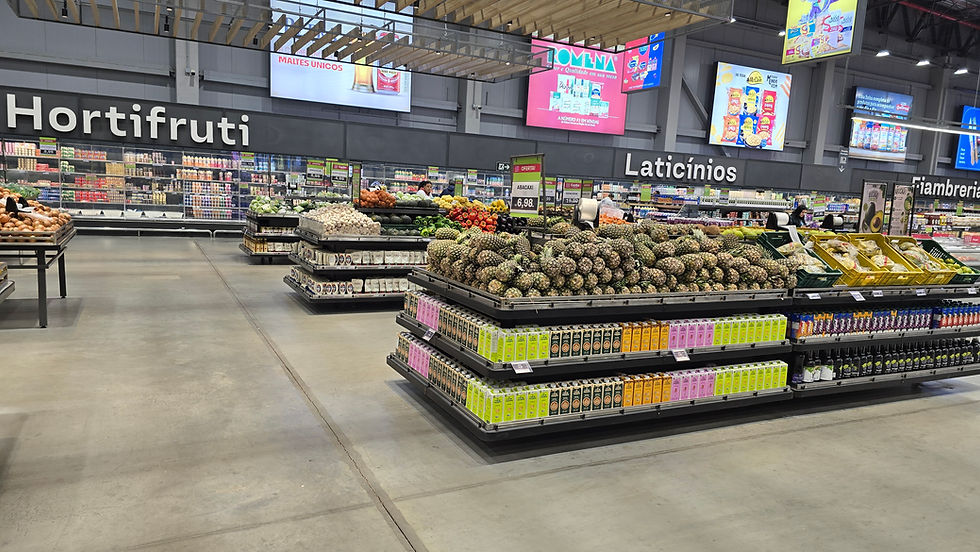 Corredor de supermercado com setor Hortifruti e Laticínios, pilhas de abacaxis e bebidas coloridas, ambiente amplo e moderno.