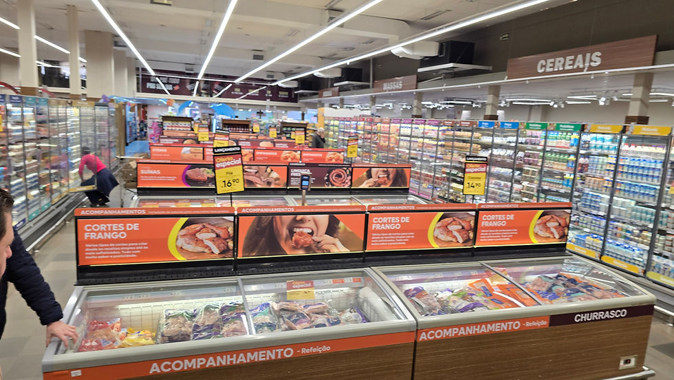 Interior de supermercado com seção de carnes e congelados, placas CEREAIS e CORTES DE FRANGO, clientes comprando.