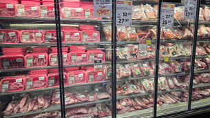 Balcão refrigerado de açougue com bandejas de carne suína embaladas em rosa e cartazes de oferta.