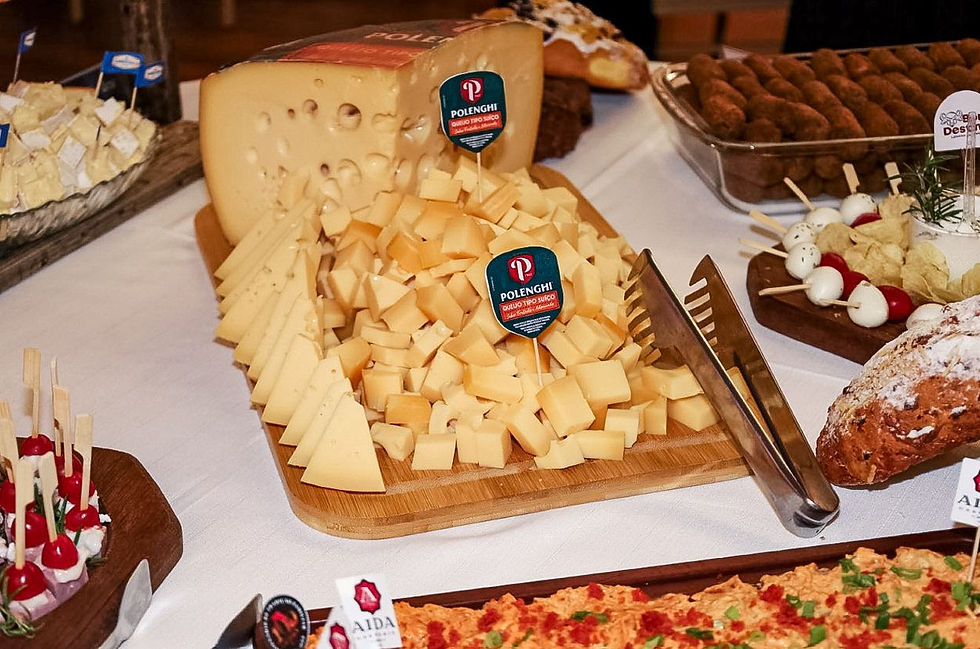 Mesa de buffet com vários queijos Polenghi em cubos e fatias, pinças metálicas e outras entradas ao fundo.
