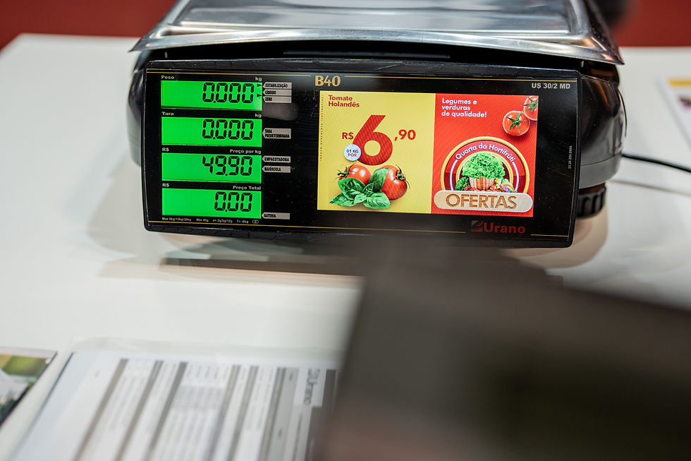 Balança digital com telas verdes exibindo peso e preço por kg de R$49,90; anúncio de tomates por R$6,90 ao lado. Fundo claro.