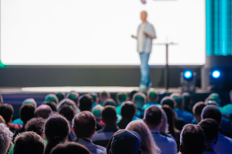 Speaker delivering a presentation to a large audience at a business conference in a modern