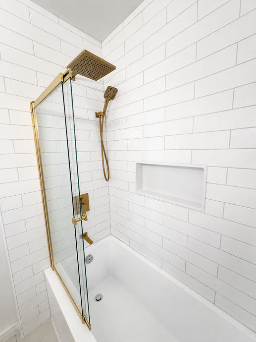 Vue de côté du bain-douche avec pommeau pluie carré doré, douchette assortie et niche dans le carrelage blanc.