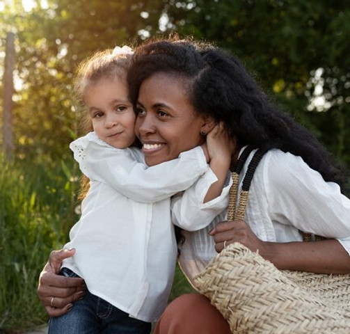 Mother and young daughter hugging outdoors in a sunny park, showing love and family bonding